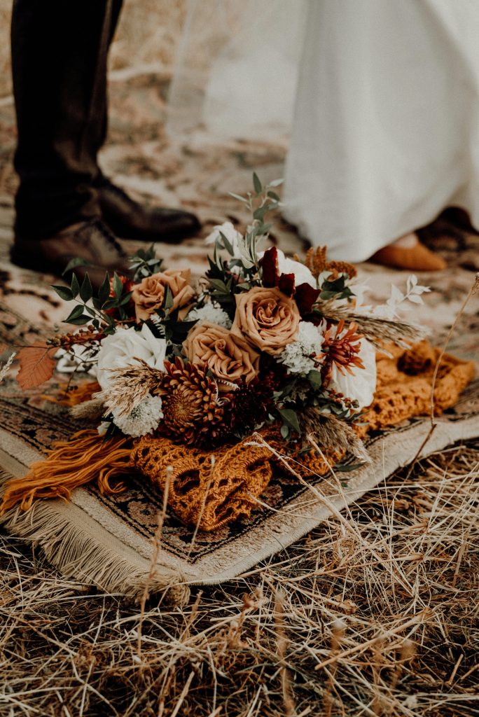 Bruidsboeket met droogbloemen op een kleed, met bruid en bruidegom op de achtergrond